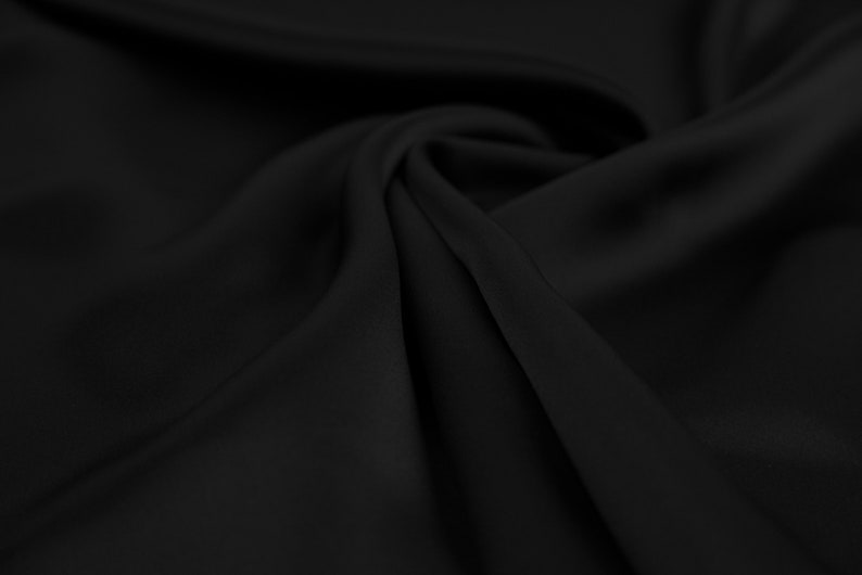 May include: Black fabric with a smooth, silky texture. The fabric is draped and folded, creating soft curves and folds.