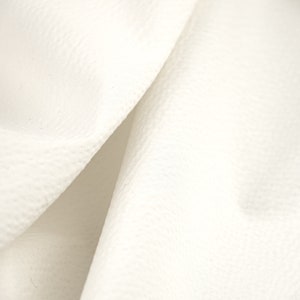 May include: Close-up of a white fabric with a textured surface. The fabric is folded in half, creating a soft, flowing look.