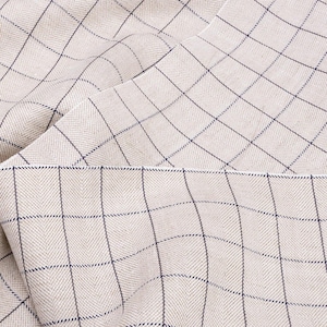 May include: A close-up of a beige fabric with a subtle herringbone weave and a grid pattern of thin blue lines.