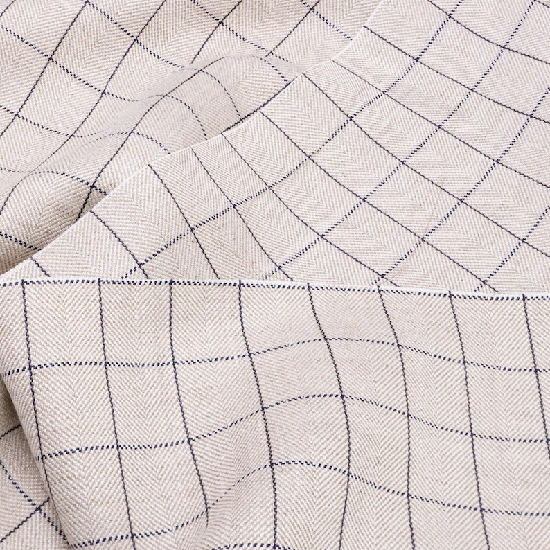 May include: A close-up of a beige fabric with a subtle herringbone weave and a grid pattern of thin blue lines.