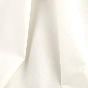 May include: Close-up of a white fabric with a textured surface. The fabric is folded and has a soft, smooth appearance.