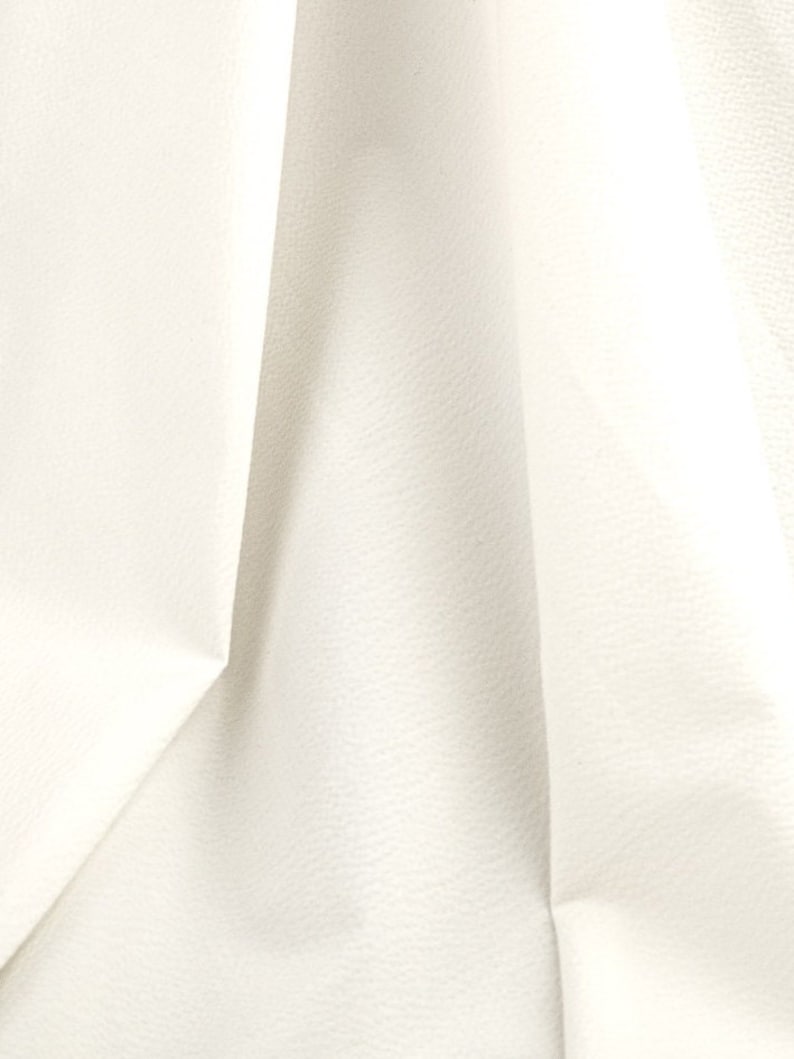 May include: Close-up of a white fabric with a textured surface. The fabric is folded and has a soft, smooth appearance.