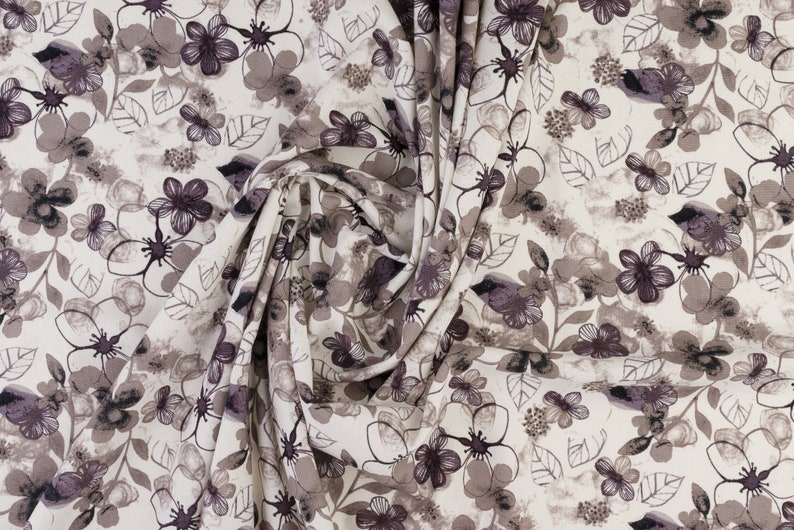 May include: A white fabric with a floral pattern in shades of brown and purple. The fabric is folded and shows the pattern repeating.