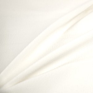 May include: White fabric with a smooth, soft texture. The fabric is folded and draped, creating a gentle curve.