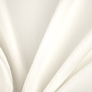 May include: White fabric with soft folds and wrinkles. The fabric is smooth and has a subtle sheen.