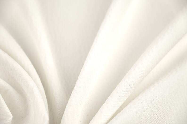 May include: White fabric with soft folds and wrinkles. The fabric is smooth and has a subtle sheen.