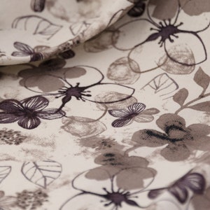 May include: A close-up of a white fabric with a floral pattern. The flowers are brown and black and have a watercolor effect. The fabric is soft and has a subtle texture.