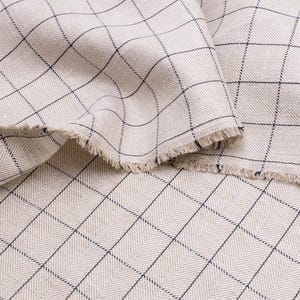 May include: Close-up of a beige fabric with a black and white checked pattern. The fabric has a slightly textured surface and a frayed edge.