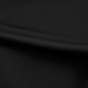 May include: A close-up of a black fabric with a smooth texture and a subtle sheen. The fabric is draped in soft folds, creating a luxurious and elegant look.