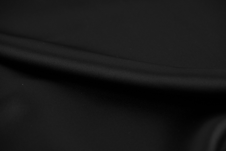 May include: A close-up of a black fabric with a smooth texture and a subtle sheen. The fabric is draped in soft folds, creating a luxurious and elegant look.