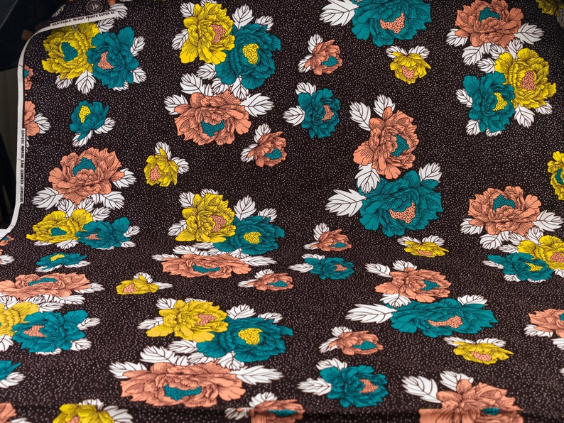 May include: A brown fabric with a repeating pattern of teal, yellow, and peach flowers. The flowers have white outlines and are set against a dark brown background with a subtle white speckled pattern.
