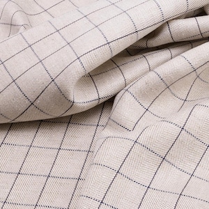 May include: A close-up of a beige fabric with a fine herringbone weave and a dark blue checkered pattern.