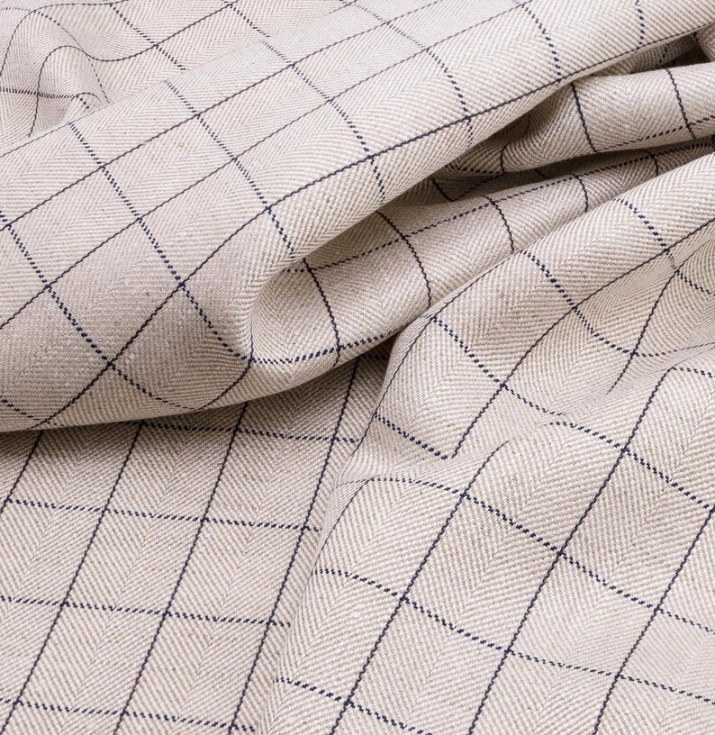 May include: A close-up of a beige fabric with a fine herringbone weave and a dark blue checkered pattern.