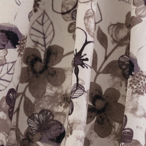 May include: Close-up of a white fabric with a brown and black floral pattern. The fabric is folded and the pattern is visible on both sides of the fold.