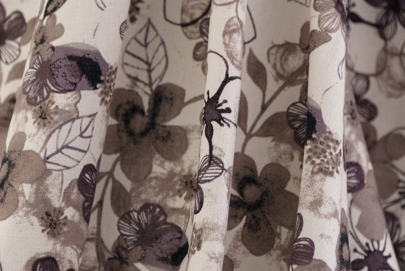 May include: Close-up of a white fabric with a brown and black floral pattern. The fabric is folded and the pattern is visible on both sides of the fold.