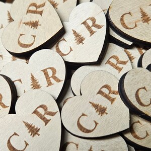 May include: A pile of wooden heart-shaped ornaments with the letters "CAR" and a small pine tree design engraved on each one.