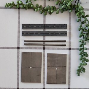 Puede incluir: Un conjunto de piezas met&aacute;licas para un proyecto de bricolaje. El conjunto incluye dos barras met&aacute;licas largas con agujeros, dos barras met&aacute;licas m&aacute;s cortas con agujeros y dos placas met&aacute;licas cuadradas con un agujero en el centro. Las placas tienen l&iacute;neas dibujadas en ellas.