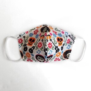 May include: White face mask with a colorful print of skeletons, guitars, and flowers. The print is inspired by the movie Coco.