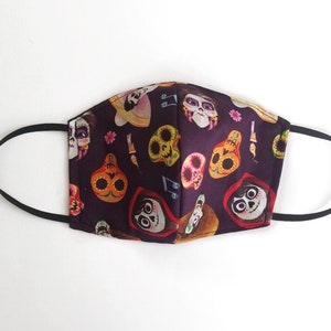 May include: A black fabric face mask with a colorful print of characters and skulls from the movie Coco. The mask has elastic ear loops.