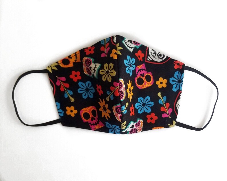 May include: Black face mask with a colorful Day of the Dead pattern featuring sugar skulls, flowers, and leaves.