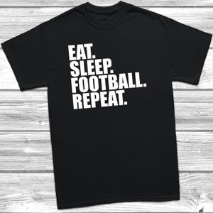 May include: Black t-shirt with white text that reads "Eat. Sleep. Football. Repeat."