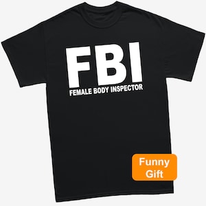 May include: Black t-shirt with the white text "FBI" above "FEMALE BODY INSPECTOR". An orange rectangle in the bottom right corner reads "Funny Gift". The shirt is a crew neck style.