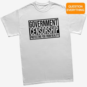 May include: A white short-sleeved t-shirt featuring a black rectangular graphic with the text GOVERNMENT CENSORSHIP PROTECTING YOU FROM REALITY. An orange rectangular tag in the upper right corner displays the text QUESTION EVERYTHING.