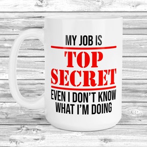 May include: White ceramic coffee mug with a black and red design. The text on the mug reads "My job is Top Secret Even I don't know what I'm doing."