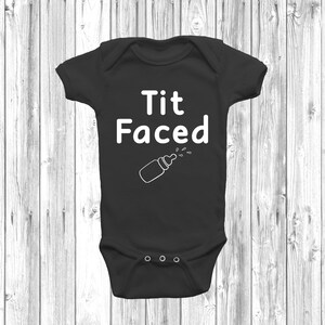 May include: Black baby grow with white text that reads "Tit Faced" and a white outline of a baby bottle with milk dripping from the nipple.