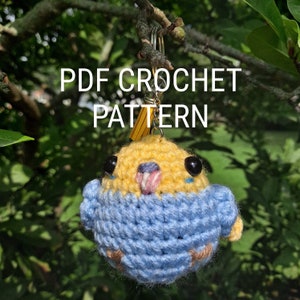 May include: A crocheted bird keychain in yellow and blue, with black bead eyes and a pink and white beak. The keychain has a yellow tassel and the text "PDF CROCHET PATTERN" in white.