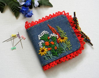 Op de afbeelding: Een naaldenkoffer van blauw denim met een rode gehaakte rand en een geborduurd bloemenmotief. De koffer heeft een gele trekkoord.