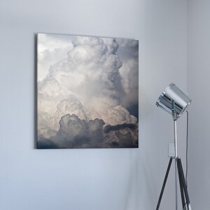 Puede incluir: Un interior de sala de estar con un sofá azul oscuro, una lámpara de trípode plateada y una fotografía enmarcada de un cielo nublado colgada en la pared.