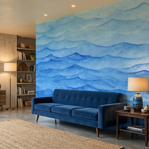 May include: A living room featuring a large wall mural with a blue watercolour wave pattern. The room includes a dark blue velvet sofa, a wooden sideboard with blue ceramic vases, a floor lamp, a side table with a lamp, and a woven area rug.