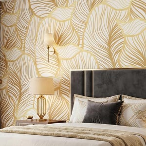May include: A bedroom featuring a dark gray upholstered bed with a matching bench, flanked by two wooden nightstands with lamps. The wall behind the bed has gold leaf-patterned wallpaper, and a large area rug covers the light wood floor.