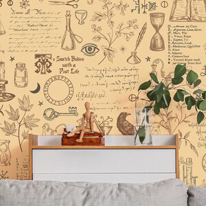 May include: A beige wall with a vintage-style wallpaper featuring a repeating pattern of alchemy symbols, plants, and handwritten text. The text includes the phrase "Search Balance with a Poet Life". The wallpaper is behind a gray couch with a green throw blanket and a vase of green plants.