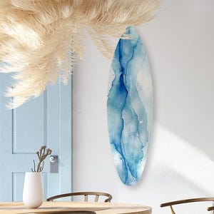 May include: A dining room scene featuring a light wood round table and six matching chairs with woven seats. A large, feathery, beige chandelier hangs above the table. A blue and white abstract art piece hangs on the white wall.