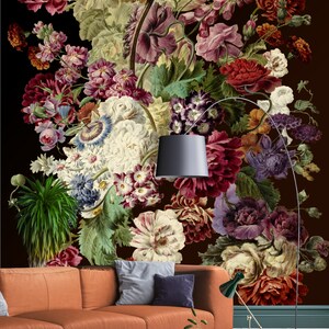 May include: A large floral arrangement with a variety of flowers in shades of red, pink, white, and purple. The flowers are arranged in a vase and are set against a dark brown background. A brown leather sofa with pillows is in the foreground.