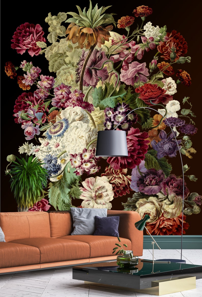 May include: A large floral arrangement with a variety of flowers in shades of red, pink, white, and purple. The flowers are arranged in a vase and are set against a dark brown background. A brown leather sofa with pillows is in the foreground.