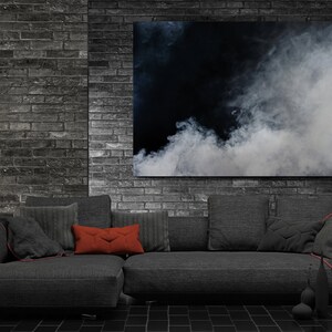Puede incluir: Un sofá seccional gris oscuro con almohadas de color rojo y gris frente a una pared de ladrillo con una gran pintura abstracta de nubes blancas sobre un fondo negro.
