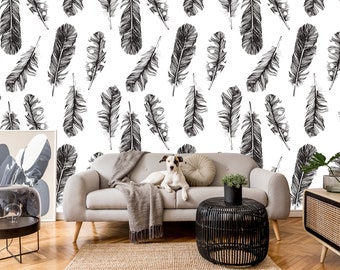 May include: A white wall with a black and white feather pattern wallpaper. A gray couch with a throw blanket and a dog sitting on it. A black side table with a potted plant and a black coffee table with a woven top.