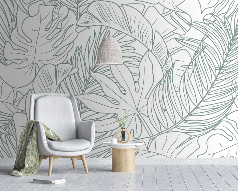 Puede incluir: Un sill&oacute;n blanco con una manta de tiro verde claro se encuentra frente a una pared con un patr&oacute;n de hojas tropicales blancas y verdes.