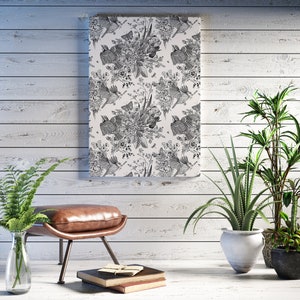 Puede incluir: Una impresión en blanco y negro de pájaros y flores sobre un lienzo, colgada en una pared de madera blanca. La impresión está enmarcada con un borde blanco. Hay un reposapiés de cuero marrón delante de la impresión y una planta en maceta a la derecha.