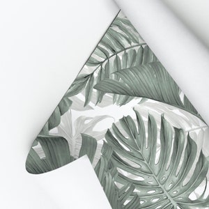 May include: A roll of wallpaper with a green and white tropical leaf pattern. The wallpaper is rolled up and partially unrolled, revealing the pattern. The text "My Wall Store" is visible in the top left corner of the image.