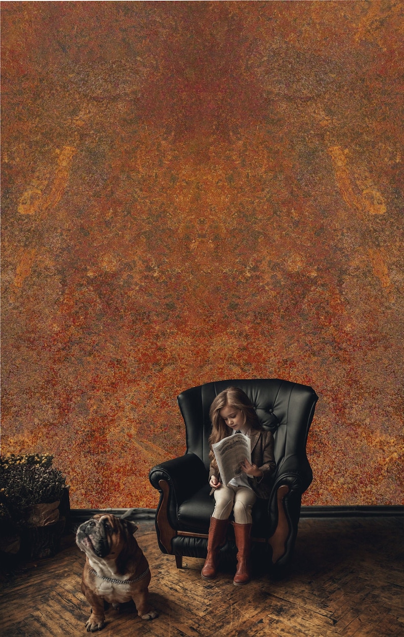 May include: A young girl sits in a black leather armchair reading a newspaper. A bulldog sits on the wooden floor in front of the chair. The background is a rusty orange wall.