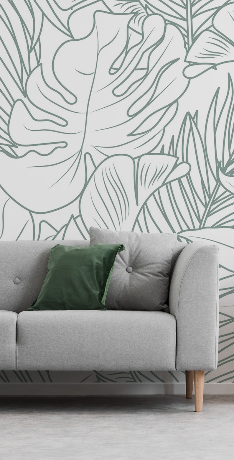 Puede incluir: Un sof&aacute; gris con dos almohadas, una verde y una gris, se encuentra frente a una pared con un patr&oacute;n de hojas tropicales blancas y verdes.