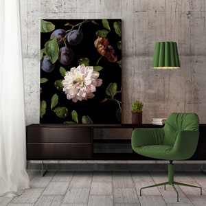 Puede incluir: Una impresión en lienzo en blanco y negro con una gran flor blanca con hojas verde oscuro y ciruelas moradas. La impresión está colgada en una pared de hormigón sobre una mesa consola de madera oscura con un sillón verde.