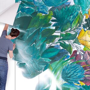 May include: A woman is applying a floral wallpaper with a watercolor design. The wallpaper features a vibrant mix of green, blue, yellow, and red botanical elements. The design includes leaves, flowers, and abstract shapes, creating a natural and artistic aesthetic.