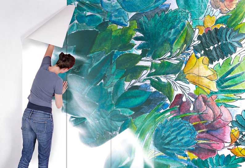May include: A woman is applying a floral wallpaper with a watercolor design. The wallpaper features a vibrant mix of green, blue, yellow, and red botanical elements. The design includes leaves, flowers, and abstract shapes, creating a natural and artistic aesthetic.