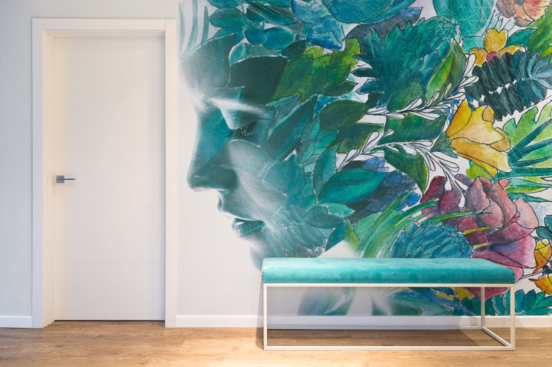 May include: A teal bench with a white metal frame sits in front of a wall mural. The mural features a woman's profile overlaid with colorful floral and leaf designs in shades of green, blue, yellow, and red. A white door is on the left.