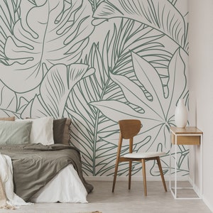 Puede incluir: Un dormitorio con una pared blanca con un dibujo de hojas tropicales en l&iacute;neas verdes. En primer plano hay una cama con un edred&oacute;n marr&oacute;n y almohadas blancas. En la esquina de la habitaci&oacute;n hay una silla de madera con un coj&iacute;n blanco. Una peque&ntilde;a mesa de madera con un jarr&oacute;n blanco est&aacute; al lado de la silla.
